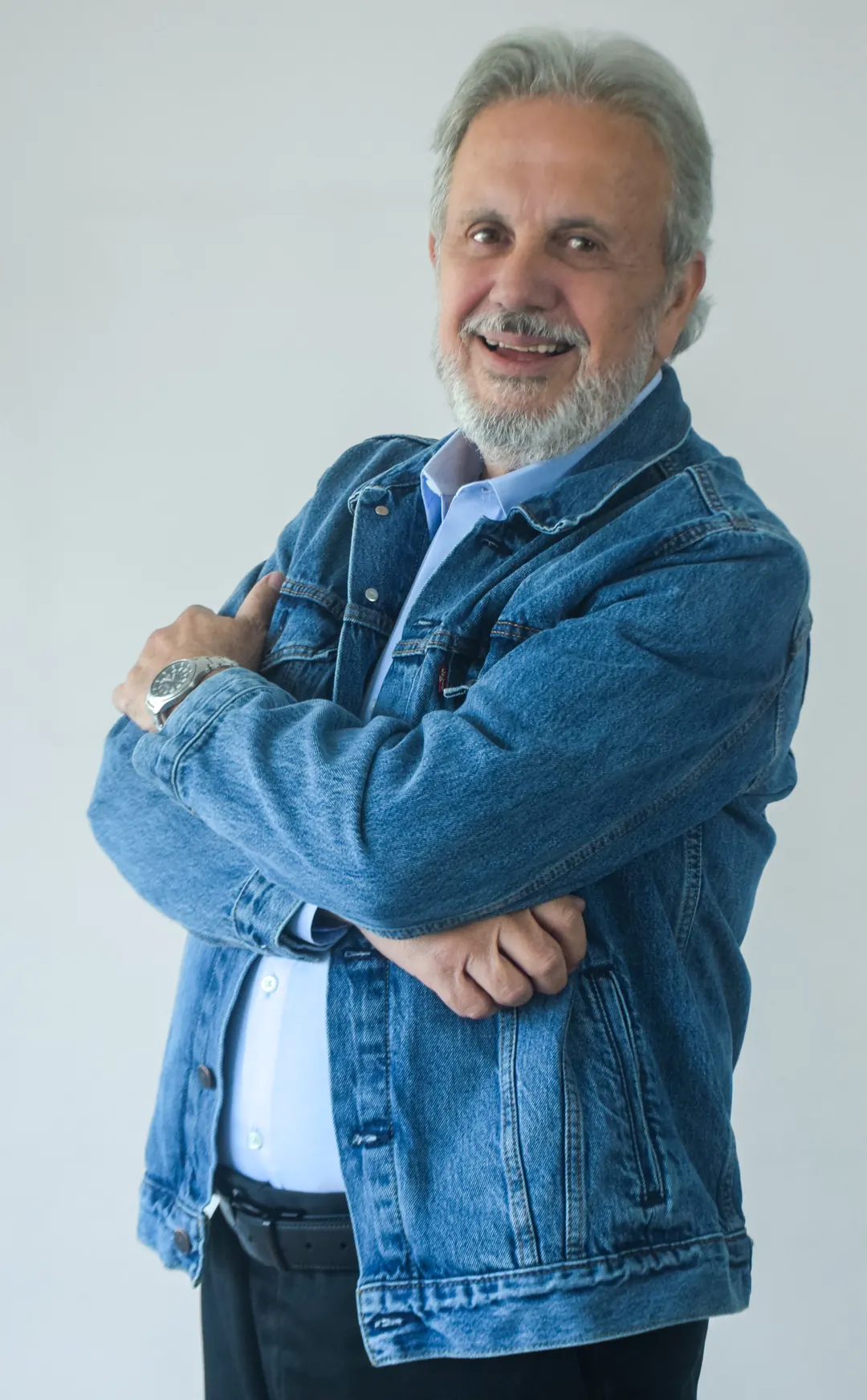 Eduardo Martí con chaqueta vaquera sobre fondo blanco, sonriendo con los brazos cruzados